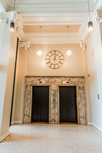 A clock hangs on the wall above a pair of black doors at Addison on Fourth Apartments, Seattle, 98104