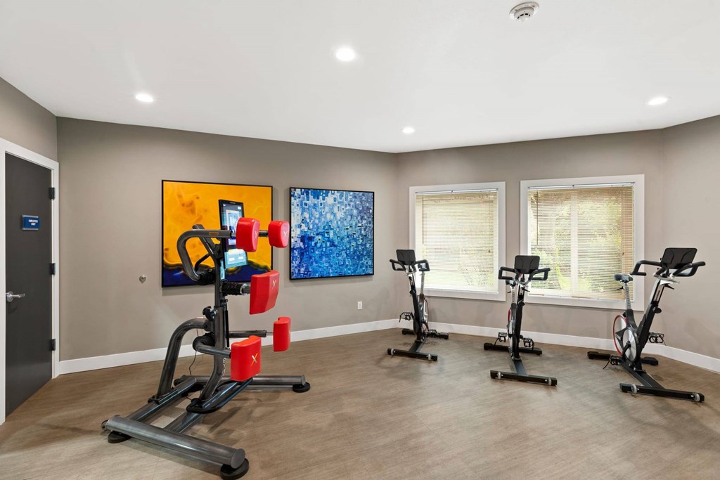 A room with a row of exercise bikes and two paintings on the wall.