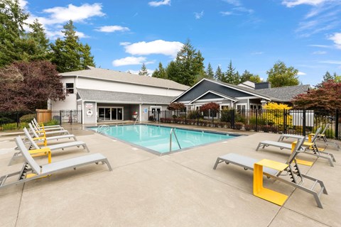 A pool with sun loungers and a building in the background.
