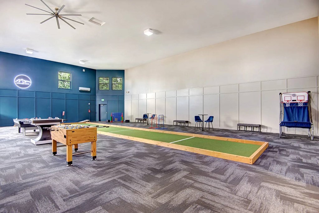 A room with a foosball table and a shuffleboard table.