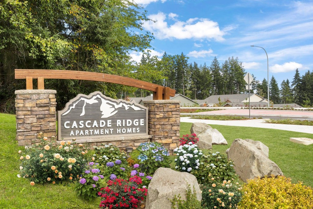 A sign for Cascade Ridge Apartment Homes is surrounded by flowers and rocks.