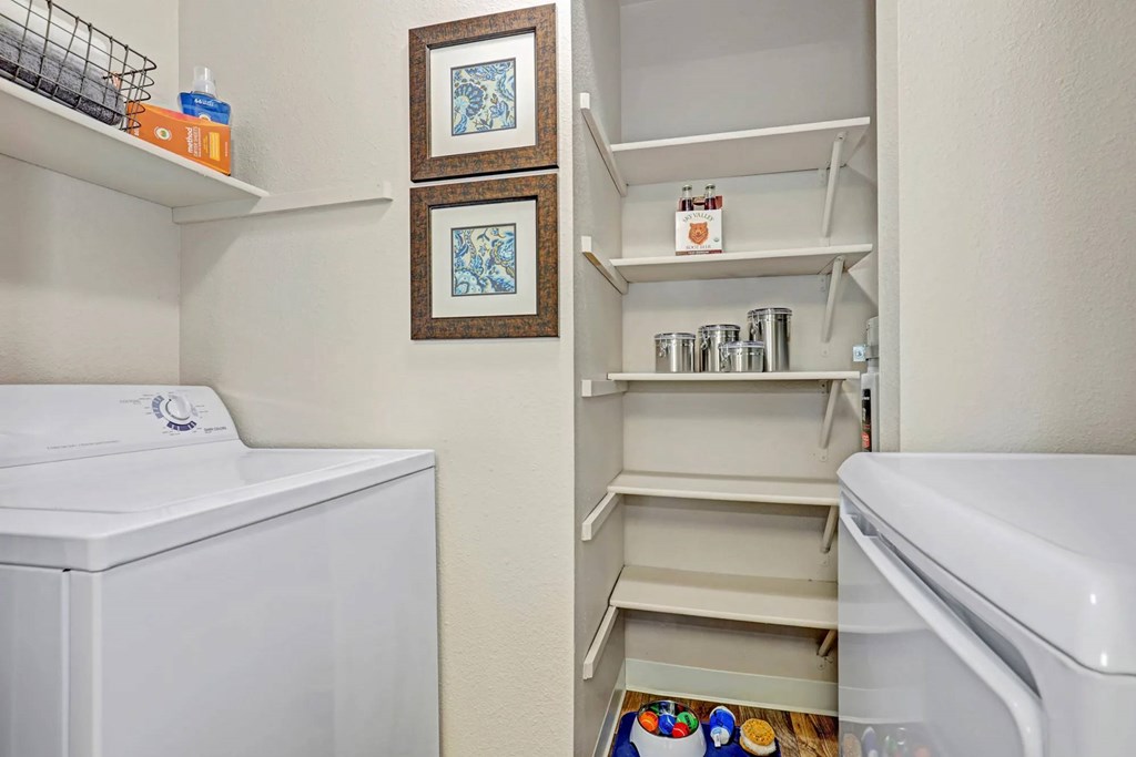 A white washing machine sits next to a white dryer in a small laundry room.