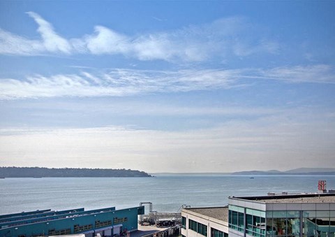 A building with a blue roof is in the foreground of a body of water with a cloudy sky above.