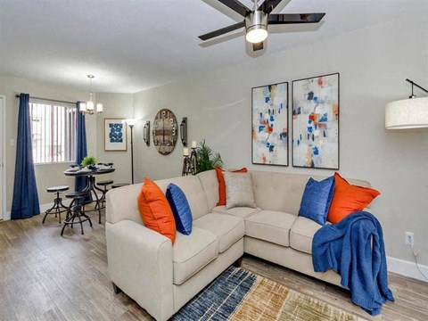 A living room with a beige couch, a ceiling fan, and a dining table with chairs.
