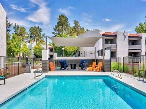 A swimming pool in front of a building with orange chairs around it.