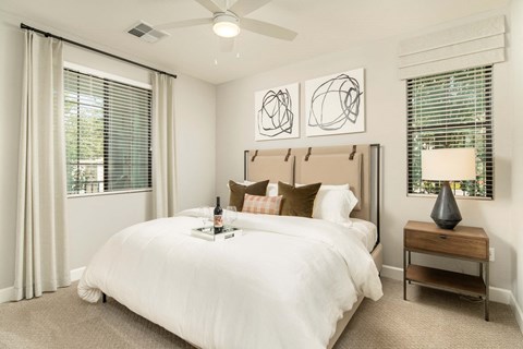 A bedroom with a large bed, a nightstand with a lamp, and two abstract art pieces on the wall.