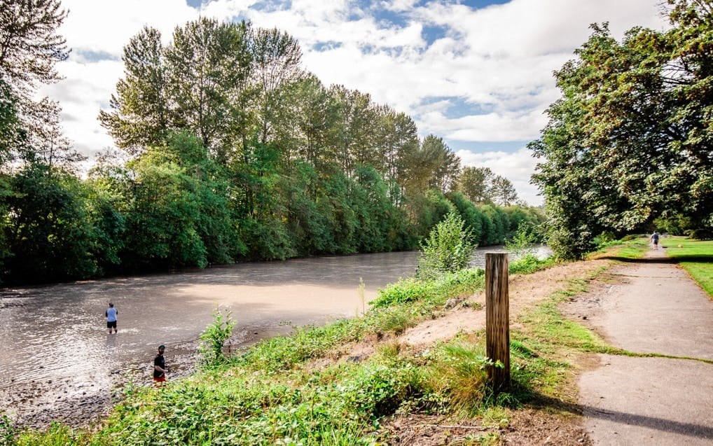 Two people are wading through a river in a natural landscape. at The Retreat, Sumner, Washington