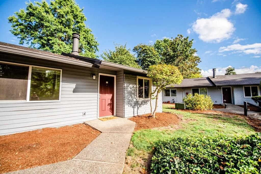 A house with a red door and a grey facade is surrounded by a green lawn and trees. at The Retreat, Sumner, 98390