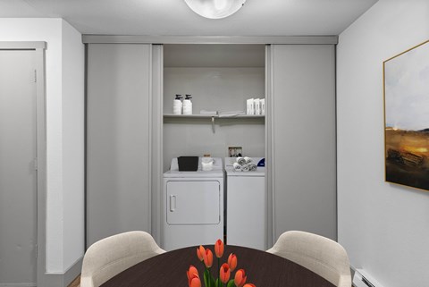 A kitchen with a dining table and chairs with a vase of red flowers on the table.