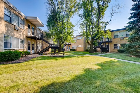 A grassy area in front of apartment buildings with a bench and trees.