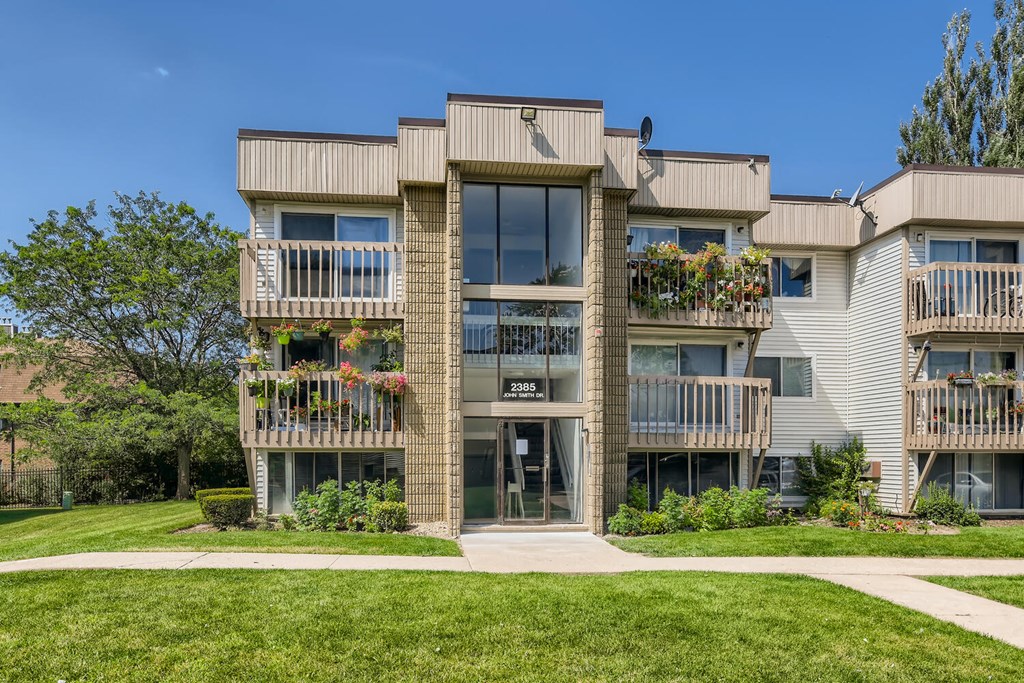 front view of an apartment building with green grass and trees