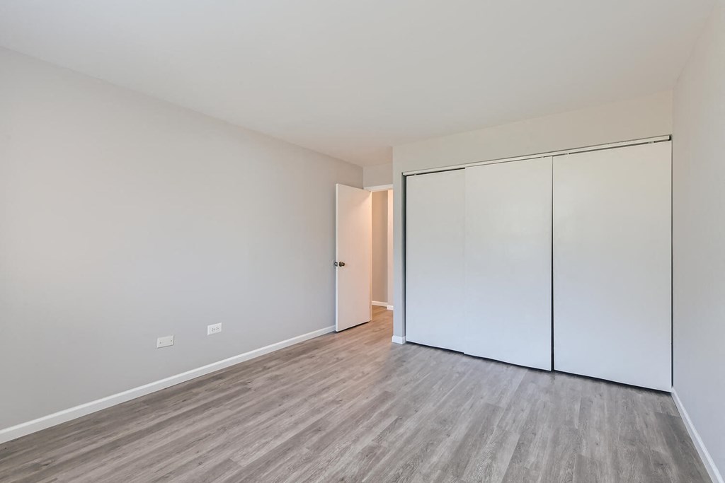 a bedroom with white walls and wood flooring and a closet