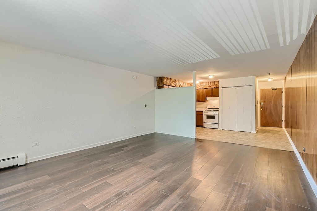 an empty living room with wood flooring and a kitchen