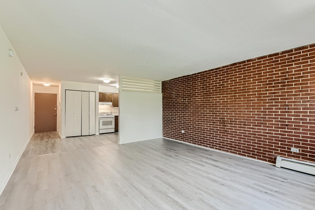 an empty living room with a brick wall and a kitchen
