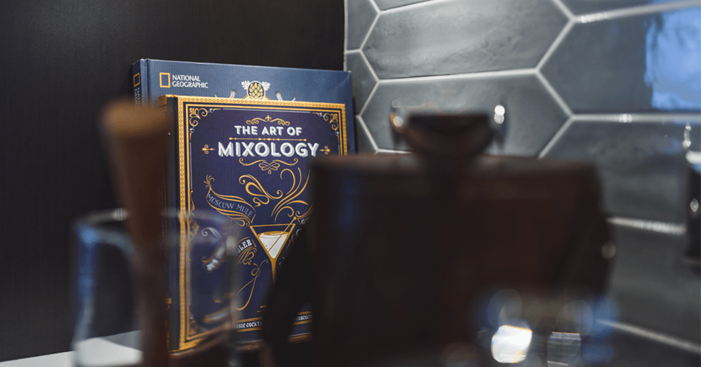 the art of mixology book on a table next to a cup of coffee