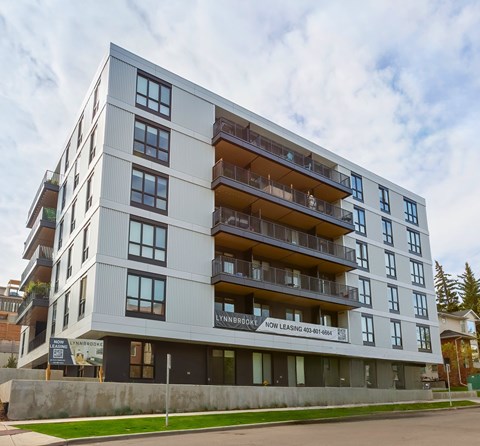 A modern apartment building with balconies and a sign that reads "Lynbrook Now Leasing".
