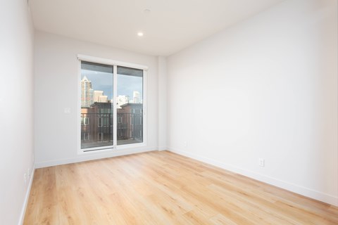 Empty room with wooden floor and a window overlooking a cityscape.