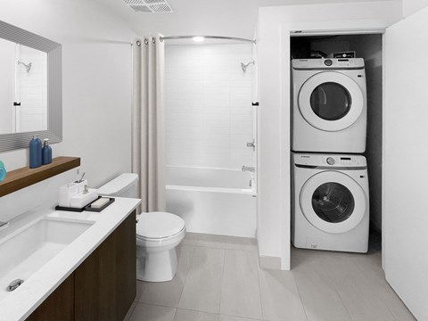 A white bathroom with a toilet, sink, and a washing machine in the doorway.
