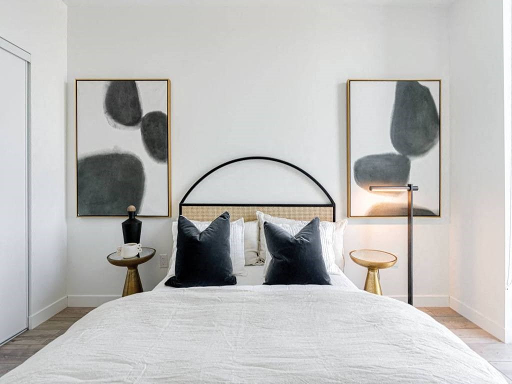 a bedroom with a bed with black and white pillows and paintings on the wall at The Village, Oakville, ON