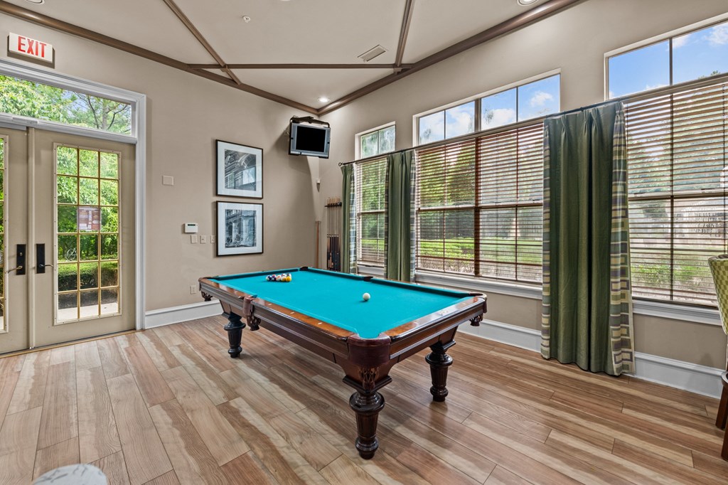 a pool table in club house with windows and a tv