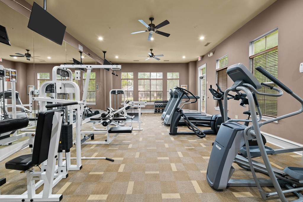 a gym with weights and cardio equipment and a ceiling fan