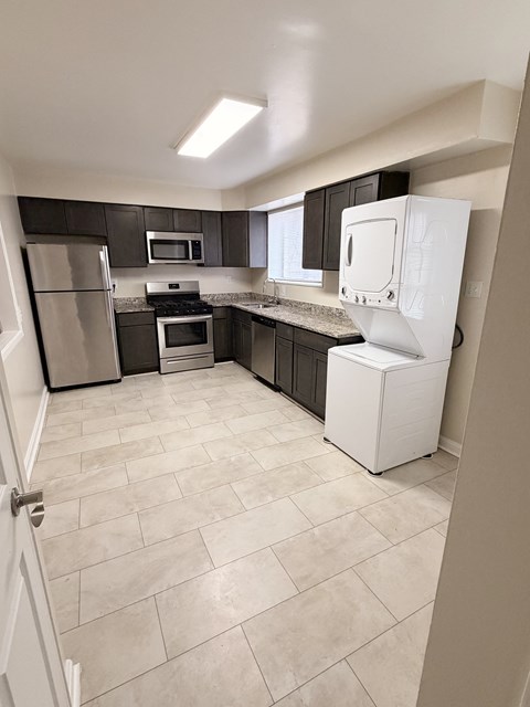 A kitchen with a white refrigerator, black cabinets, and a tiled floor.