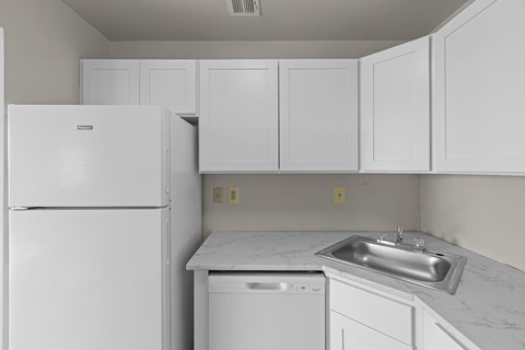 A white kitchen with a refrigerator, dishwasher, and a sink.at Kensington House, Maryland, 20895