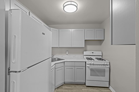 A white kitchen with a refrigerator, sink, stove, and cabinets.at Kensington House, Maryland
