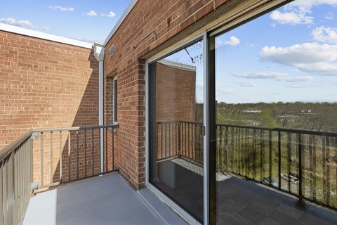 A balcony with a glass door leading to a brick building.at Kensington House, Kensington, 20895