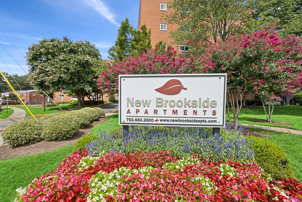 A sign for New Brookside Apartments is surrounded by flowers.