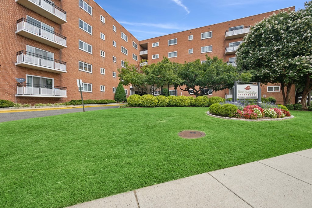 A grassy area in front of a brick building with a sign in the middle.