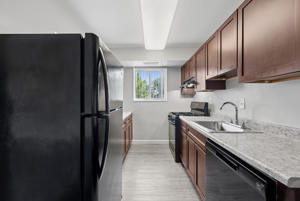 A black refrigerator is in a kitchen with brown cabinets.