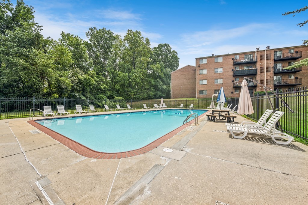 A large outdoor swimming pool surrounded by trees and chairs.