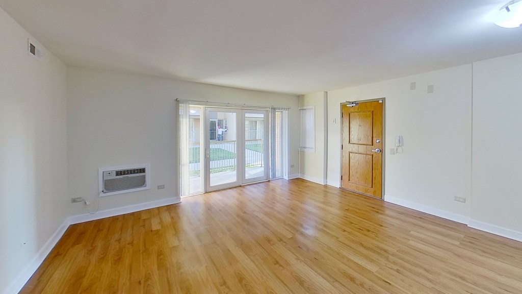 an empty living room with wood floors and a door to a balcony