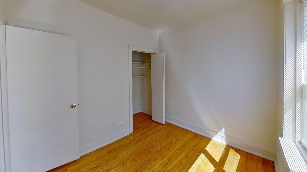a bedroom with white walls and wood floors and a closet
