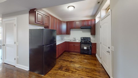 A kitchen with a black refrigerator and wooden floors.
