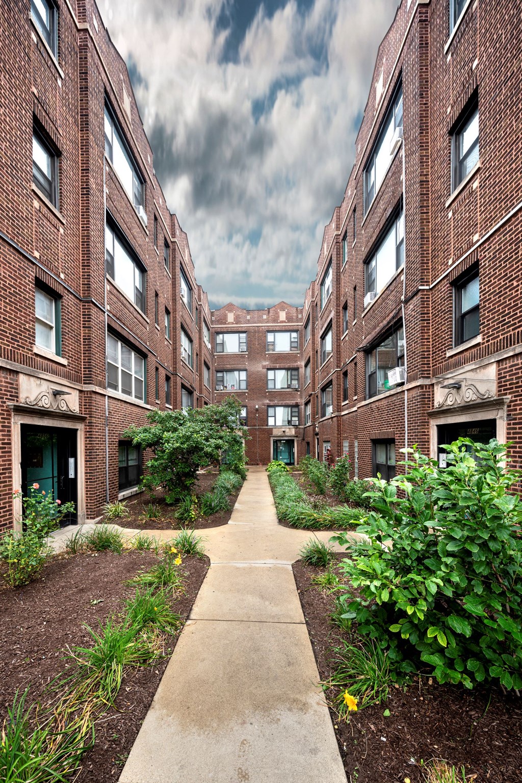 the walkway between two brick apartment buildings with a cloudy sky in the background