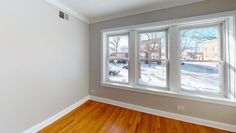 a bedroom with three windows and a wood floor