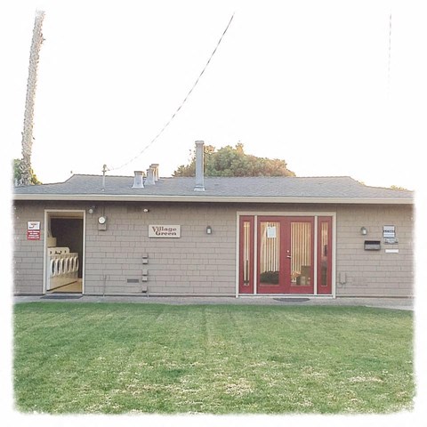a brick building with red doors and a grass yard
