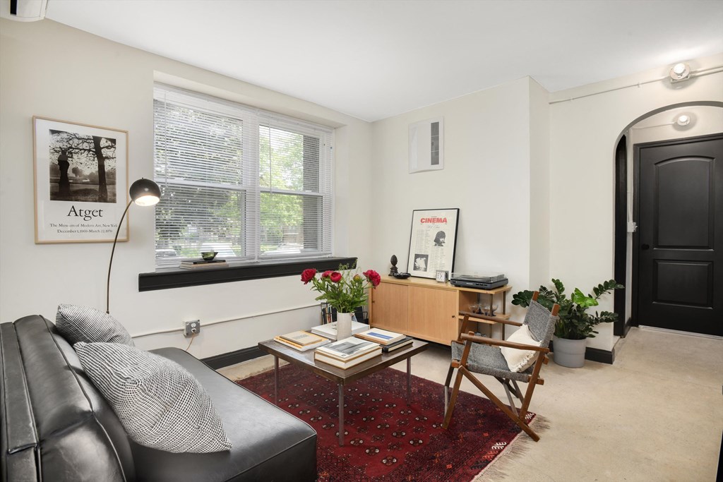 a living room with a black leather couch and a desk and a window