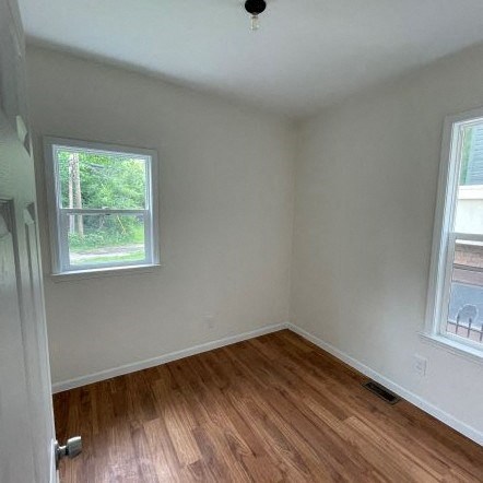 an empty room with a wooden floor and two windows