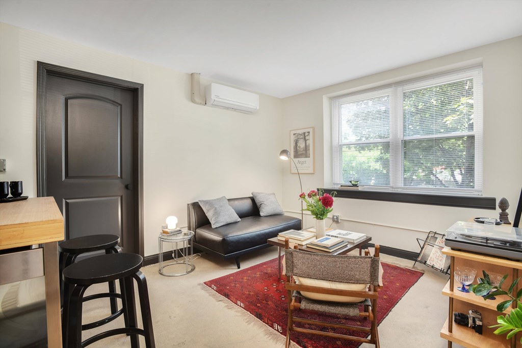 A living room with a black door, a couch, a chair, a table, and a window.