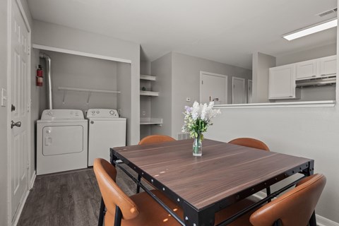 A kitchen with a table and chairs in the foreground and a refrigerator and cabinets in the background.