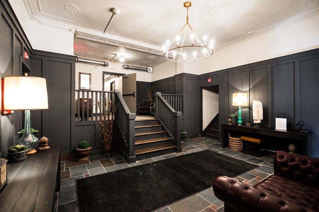 A large brown leather couch sits in a room with a staircase and a chandelier.