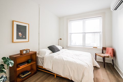 A bedroom with a bed, nightstand, and a window.