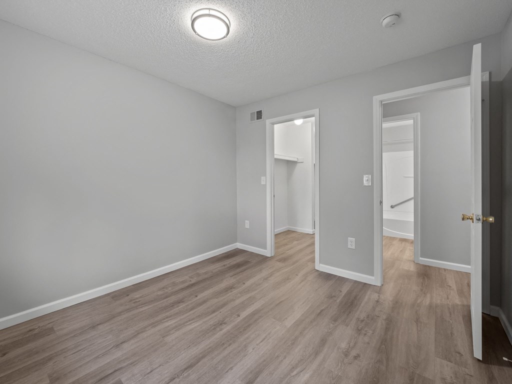 the living room of an apartment with wood flooring and a door to the bathroom