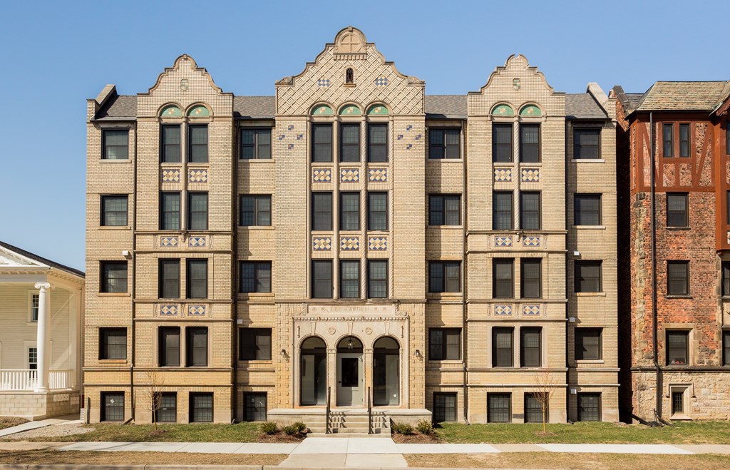 A large, beige, multi-story building with a balcony and arched doorways.