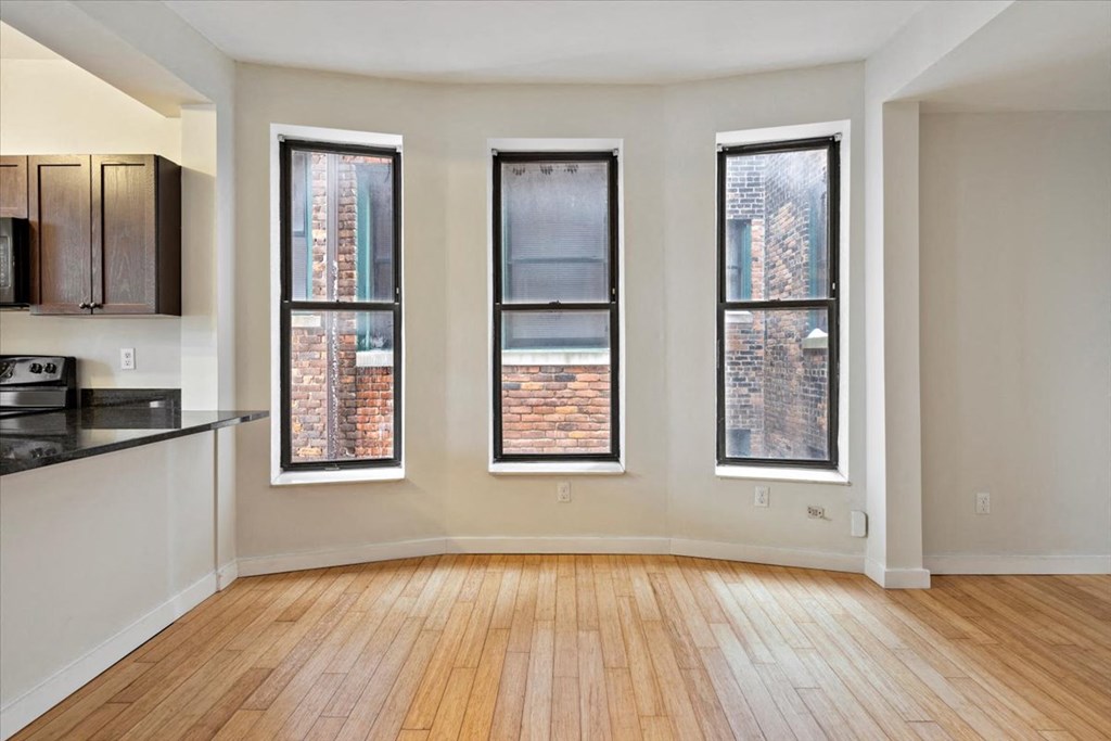 an empty living room with three windows and a kitchen in the background