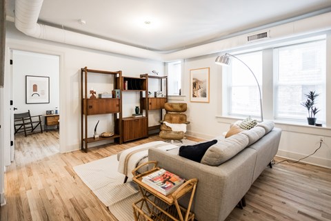 A living room with a grey couch, a wooden coffee table, and a large window.