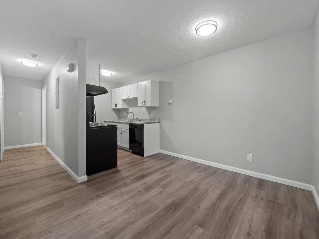 the living room and kitchen of an apartment with white walls and wood floors